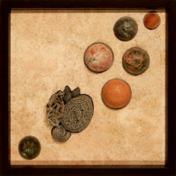 Earth Sampler IX: Pyrite Vignette<br>
13" x 13", 2014 <br>
Travertine; pyrite concretion, barite crystal with pyrite; fossil gastropods & ammonite; spheres of carnelian, marble, unakite, sunstone, jasper, labradorite A group of objects on the ground with a picture frame.