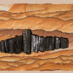 Tourmaline Titans <br>
23" x 9", 2017 <br>
Kanab sandstone, black tourmaline, black quartz geode A painting of rocks and mountains in the background.