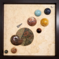 Earth Sampler Series XXV: Flash Gordon <br>
13" x 13", 2019 <br>
Fossiliferous limestone; Turee Creek rhyolite; spheres of: dumortierite, amazonite, silicified porcelainite, banded dolomite, red tiger’s eye, jasper, labradorite; gypsum rose, red ammonite (Cleoniceras besairei), metal Interstellar explorer A picture of some planets in the middle of a wall.