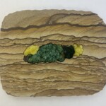 Pocket XXVII: Blooms in the Desert <br>
9.125 x 11.375”, 2023 <br>
Blooms in the Desert is a piece of stone art created using picture sandstone from Kanab, Utah which is inlaid with rare mineral specimens. The tiny crystal on the left is one of the Tabasco geodes from Zacatecas, Mexico which are the tiniest geodes in the world. The electric yellow brucite crystals from Pakistan are an extraordinarily rare color which reminds one of the yellow blooms on prickly pear cactus. The “prickly” green crystals are beautiful malachite from central Africa. A picture of a piece of art that is made out of clay.