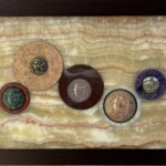 Tidal Remains <br>
7.19" x 10.38" x 2.00", 2024 (September) <br>
Banded onyx; cuprite with chrysocolla, traventine, marble, charoite; jasper, orbicular jasper, rose quartz, and aventurescent feldspar A picture of some coins in a frame.