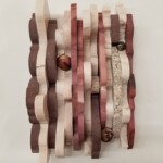 Waves I: Claret Cresting <br>
5.5” x 9”, 2018 <br>
Marble, mookaite, syenite, mookaite spheres, fossiliferous limestone cabochon A close up of a wooden sculpture with different colored strips
