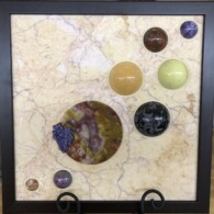 Earth Sampler Series XXVII: Petrified Blooms <br> 13”x 13”, 2021 <br> Marble; Petrified wood; spheres of: charoite, brecciated jasper, serpentinite, calcite, gabbro, ruby in matrix, jasper; botryoidal amethystine chalcedony spherules A picture of some different colored stones on the wall.