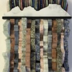 Waves XVIII: Rainbow Butte <br> 8.25” x 5.75”x 2.0”, 2022 <br> Discs: rose quartz, aventurine, rhodonite, lapis lazuli, amethyst, dumortieritic quartzite, jasper
Slabs: marble, gabbro, dumortieritic quartzite, granite, limestone, sodalite syenite A wall hanging made of rocks and wood.