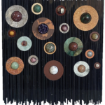 Floating: Inside the Straight and Narrow Life – 19.25” x 17.25” x 2.25”, 2023 <br>Slabs of marble, travertine, limestone, onyx, ferruginous silicified shale (printstone), slate, fuchsite chert; spheres of red jasper, fuchsite and ruby, jasper and agate, chrysocolla and cuprite, gold jasper, silicified porcelanite (mookaite), ocean jasper, amethyst, ferruginous silicified shale (printstone), jade, rhodonite, white jasper, sunstone; crystals of amethyst, gypsum A black wall with many different colored circles
